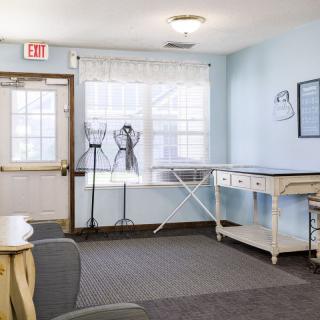 A bright room with light blue walls, featuring a table, chairs, and a large window allowing natural light to illuminate the space.