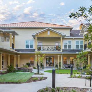 A two-story residential building with a courtyard and landscaped surroundings under a partly cloudy sky.