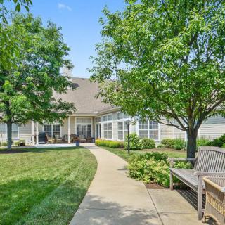 A serene garden path leading to a building, surrounded by lush greenery and benches.