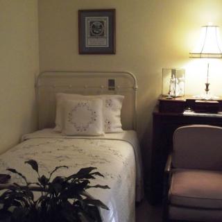 A cozy bedroom with a single bed, a nightstand with a lamp, and an armchair.