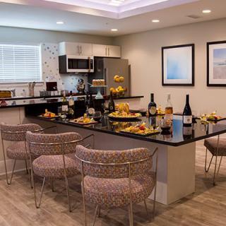 A modern kitchen and dining area with sleek countertops, bar stools, and a table adorned with wine bottles and fruit.