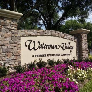 Entrance sign for Waterman Village, a premier retirement community, surrounded by vibrant flowers.