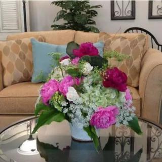A vibrant floral arrangement sits on a glass table in a cozy living room.