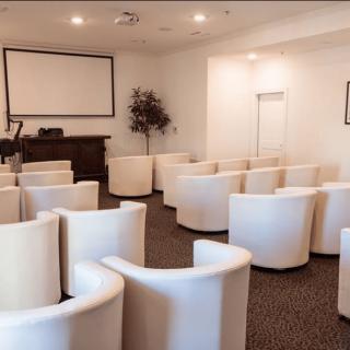 A conference room with white chairs arranged facing a projector screen.