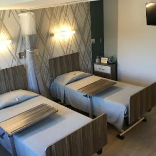 A modern hospital room featuring two twin beds with bedside tables and stylish wall lighting.