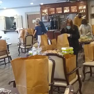 A community gathering in progress with attendees preparing food and organizing lunch bags.