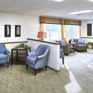 A modern waiting room with blue chairs, a small table, and large windows allowing natural light.