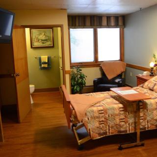 A cozy hospital room with a bed, TV, and large windows providing natural light.