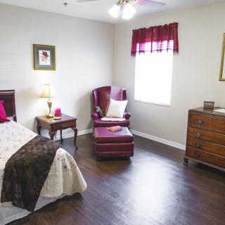 A cozy bedroom with a bed, armchair, and dresser.