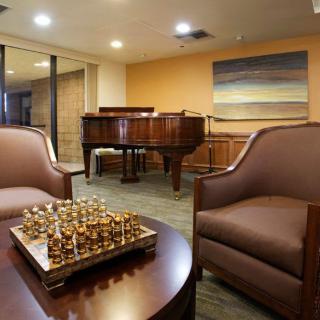 A cozy living room with a grand piano, a chessboard on the table, and comfortable chairs.