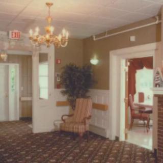A cozy lobby with a chandelier and armchair, featuring a patterned carpet and doorway leading to another room.