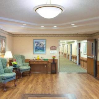 A cozy waiting area with chairs, a table, and a painting on the wall, leading to a hallway.