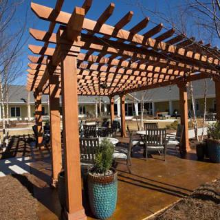 A wooden pergola with outdoor seating and potted plants on a sunny patio.