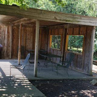 A rustic wooden shelter with seating, surrounded by nature.