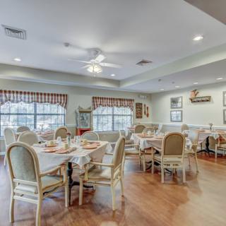 A cozy dining room setup with multiple tables and chairs, featuring large windows and decorative elements.