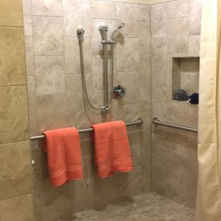 A walk-in shower with tiled walls and orange towels hanging on a bar.