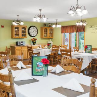 A cozy restaurant dining area with neatly arranged tables and chairs, decorated with flowers and illuminated by overhead lamps.