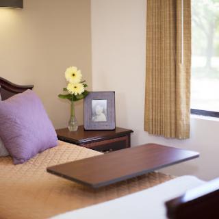 A cozy bedroom setup featuring a neatly made bed, a vase of flowers, and a picture frame on the nightstand.