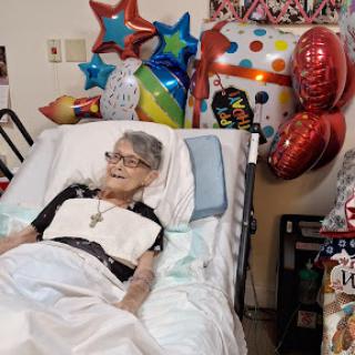 An elderly patient surrounded by colorful balloons, celebrating a special occasion.