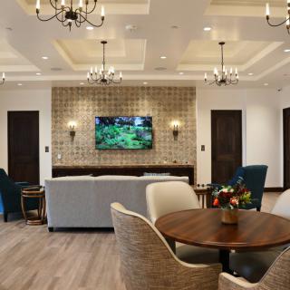 A modern living room featuring comfortable seating, a wall-mounted television, elegant chandeliers, and a cozy round table.