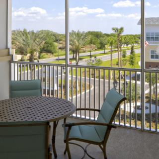 A cozy balcony with a table and chairs overlooking a scenic, tree-lined residential area.