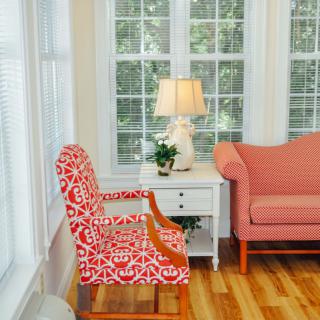A cozy living room corner with a patterned chair, sofa, and a lamp by the window.