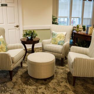 A cozy seating area featuring three armchairs, an ottoman, and a small round table with plants and decorative pillows.