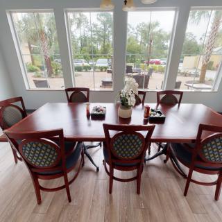 A dining area with a wooden table surrounded by chairs, featuring large windows that let in ample natural light.