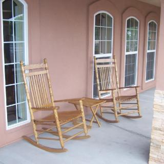 Two wooden rocking chairs sit on a porch in front of large windows.
