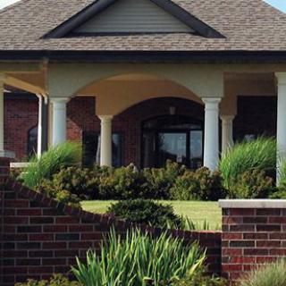A brick house featuring a covered porch with columns and landscaped front yard.