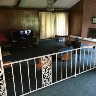 A cozy living room with wood paneling and a carpeted floor, featuring a TV and a fireplace.