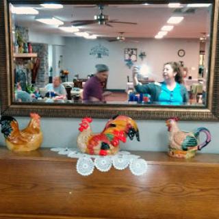 A lively dining area featuring decorative chickens on a wooden table and reflections in a mirror.