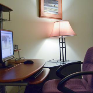 A cozy office space with a computer desk, monitor, and lamp.