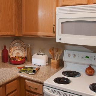 A cozy kitchen with wooden cabinets, featuring a microwave, oven, and a toaster on the countertop.