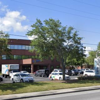 A modern office building surrounded by trees and parked vehicles on a sunny day.