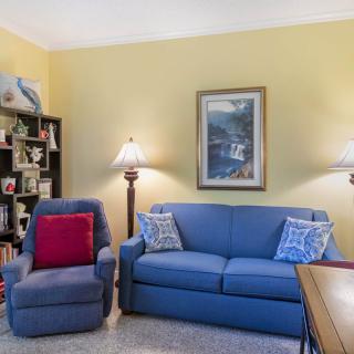 A cozy living room featuring a blue sofa and armchair, complemented by decorative lamps and a bookshelf filled with various items.