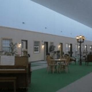 A spacious indoor hallway of a hotel with a piano, tables, and chairs lining the path.