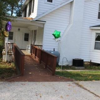 A white house with a wooden ramp leading to the entrance, adorned with colorful balloons.