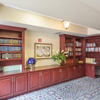 A cozy library corner with wooden bookshelves filled with books, a vase of flowers, and decorative items on the cabinets.