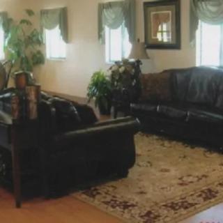 A cozy living room with leather sofas, a decorative carpet, and large windows adorned with curtains.