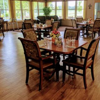 A cozy dining area with neatly arranged tables and chairs, surrounded by large windows and wooden flooring.