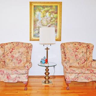 A cozy living room setup with two floral armchairs and a glass-top side table adorned with a lamp and decorative items.