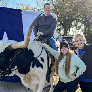 A fun day outdoors with family, riding a bull against the backdrop of a Texas flag.