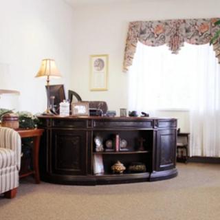 A tidy office space with a wooden desk, lamp, and window with floral curtains.