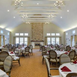 A spacious and elegantly decorated dining room with neatly arranged tables and chairs, featuring a grand fireplace and large windows.