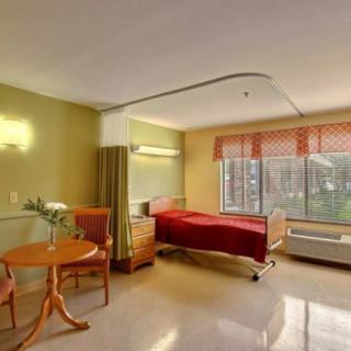 A clean and well-lit hospital room featuring a patient bed, table, and large window.