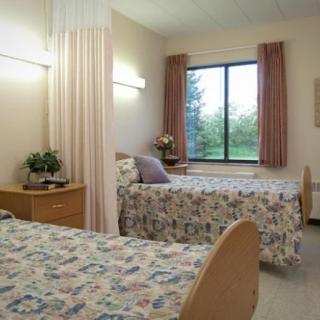 A hospital room with two beds, bedside tables, and a window overlooking greenery.