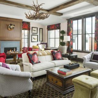A stylish living room with elegant furniture and decor, featuring a central fireplace and antler chandelier.