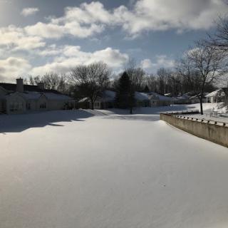 A serene winter landscape covered in fresh snow, under a partly cloudy sky.