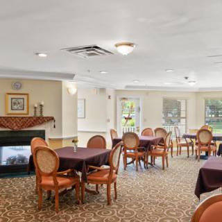 A cozy dining room with elegantly set tables, a fireplace, and large windows overlooking greenery.
